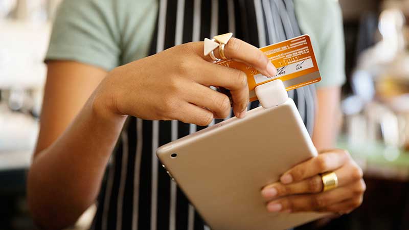 A waitress swipes a Visa card through a Square reader attached to a tablet. A waitress swipes a Visa card through a Square reader attached to a tablet.