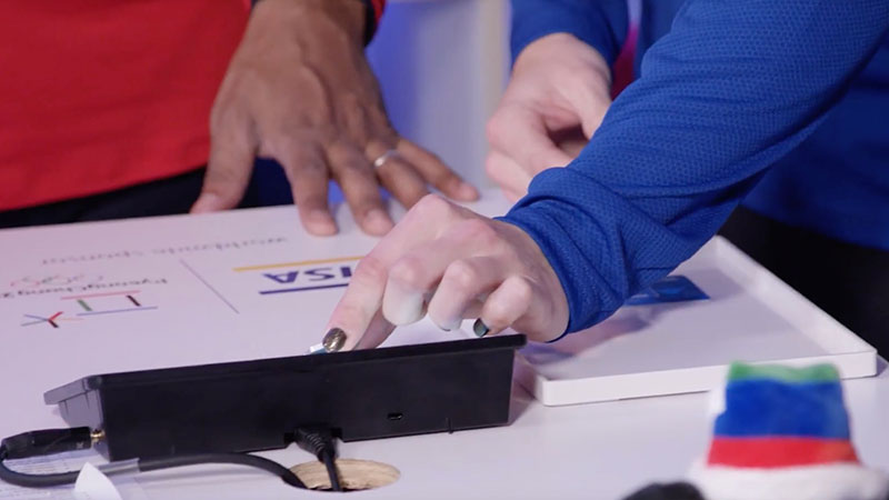 Two people stand around a table to test out a Visa wearable innovation. 