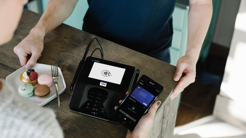 Person holding a mobile phone with a Visa card visible on screen while in front of a payment terminal.